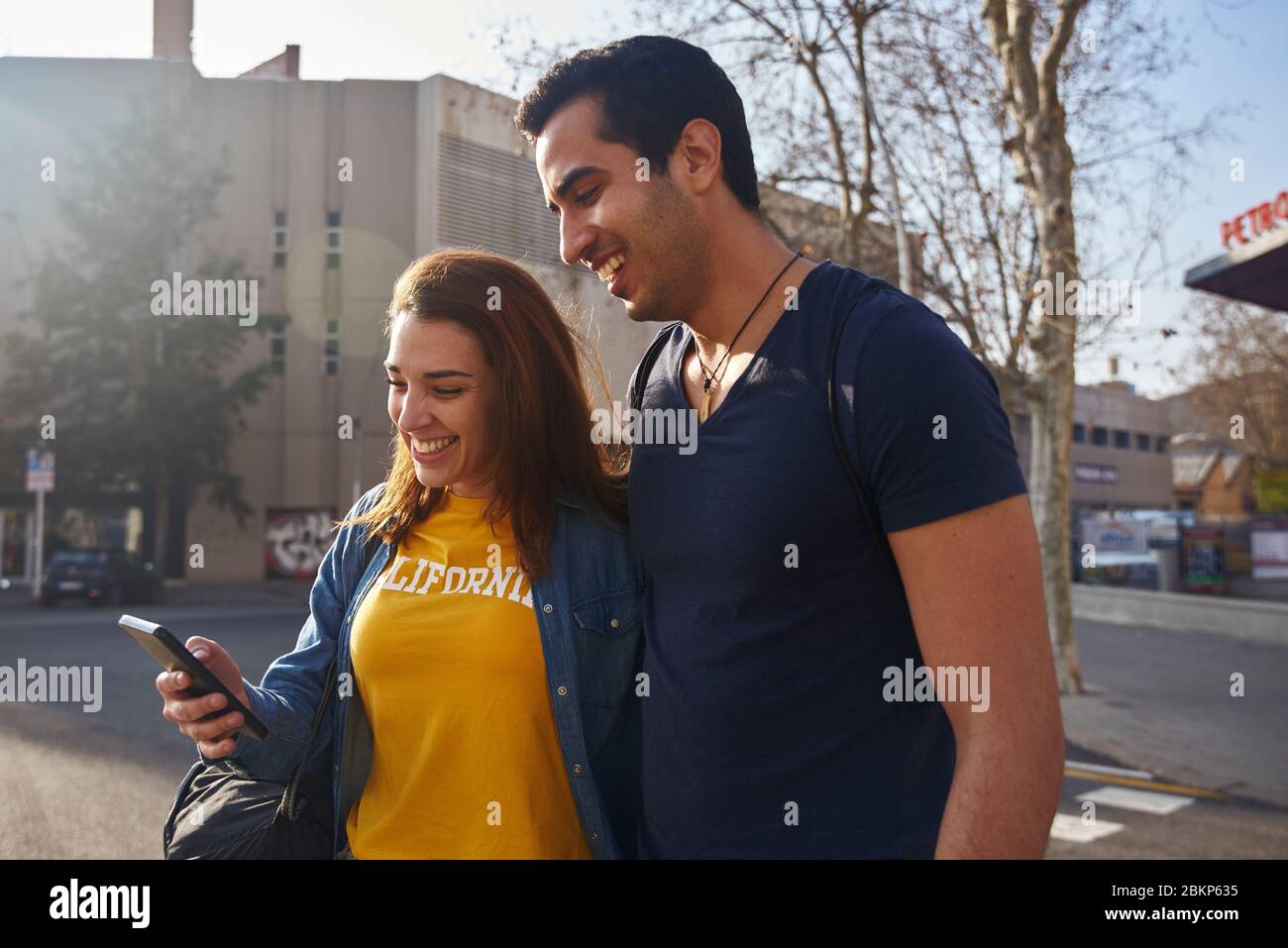 Un couple qui marche dans une ville en regardant un téléphone mobile et souriant. Banque D'Images