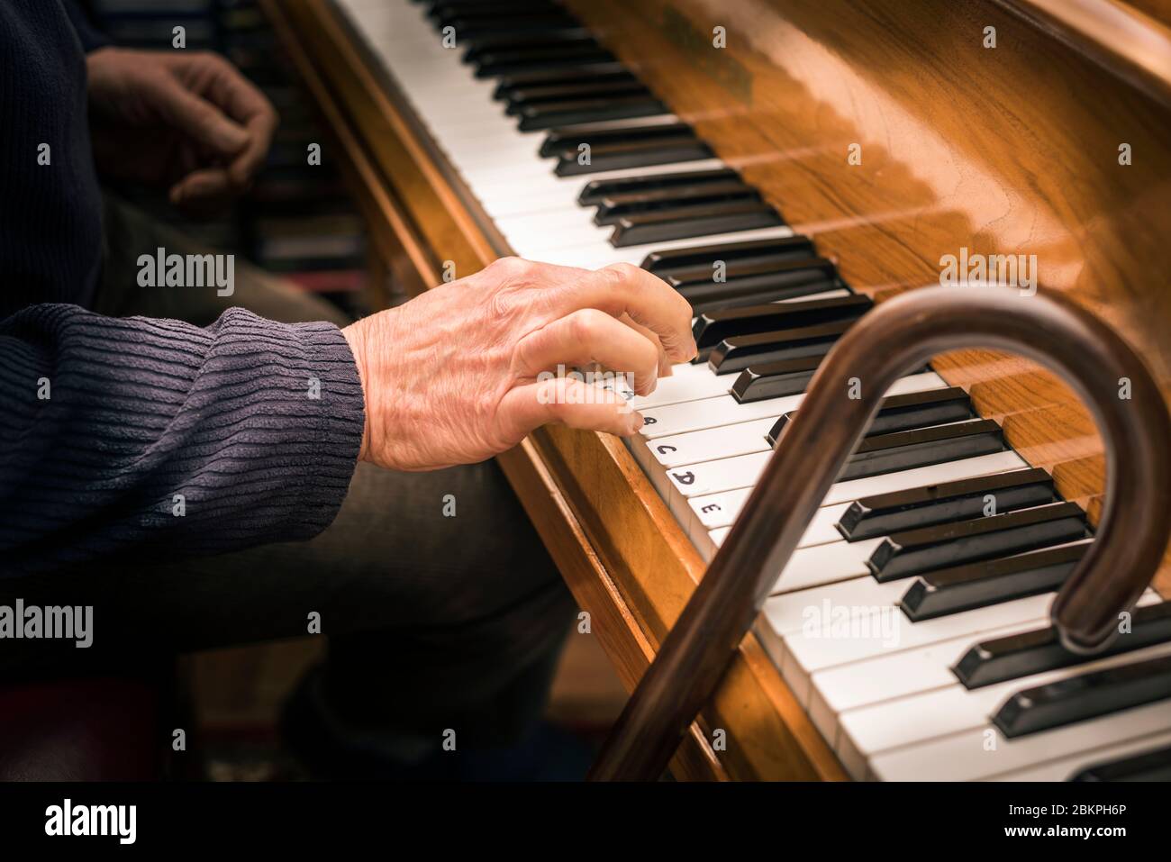 Main d'un homme âgé au piano et bâton de marche ayant une leçon de piano. Concept: Activité de vieillesse, stimulation, apprentissage, jamais trop vieux, maintien jeune. Banque D'Images
