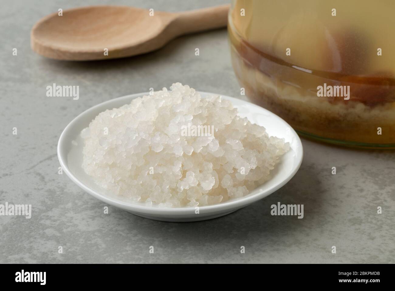 Bol avec grains de kéfir d'eau probiotique bio devant un pot en verre rempli de grains et de fruits Banque D'Images