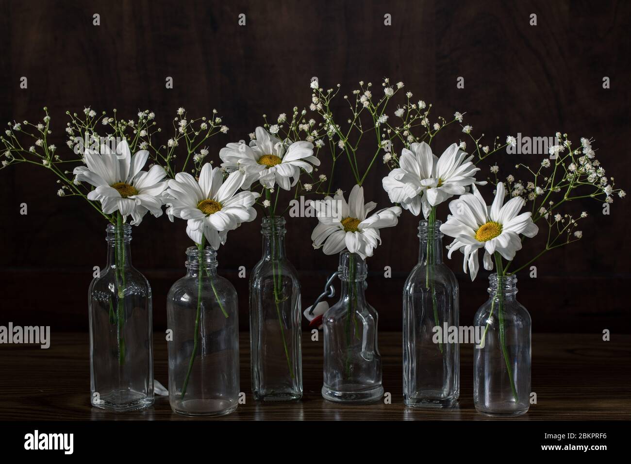 pâquerettes et fleurs de bébé dans de petites bouteilles, fond sombre encore-vie, table décorative Banque D'Images