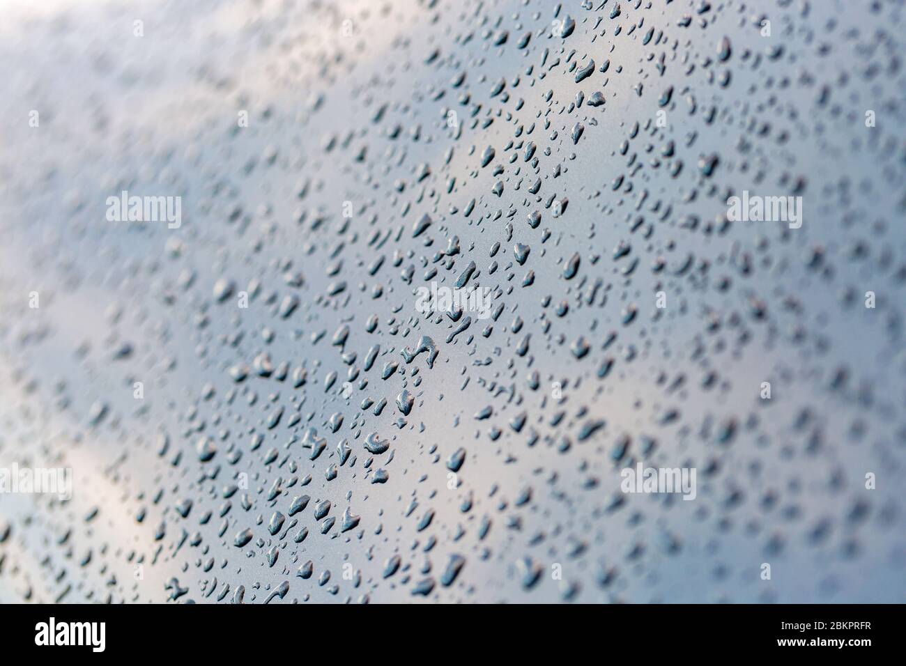 Gouttes de pluie scintillantes sur la surface de la voiture. Ciel réfléchi. Arrière-plan abstrait. Photo sélective. Banque D'Images