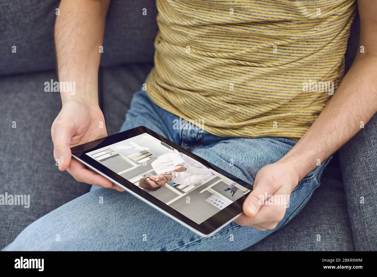 Consultation médicale en ligne pour les patients. Un médecin/homme appelle en vidéo avec une tablette avec un patient assis sur le canapé à la maison. Banque D'Images