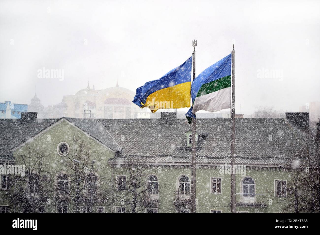 Drapeau national ukrainien et drapeau municipal de la ville de Rivne flottant dans le vent pendant la chute de neige contre les bâtiments Banque D'Images