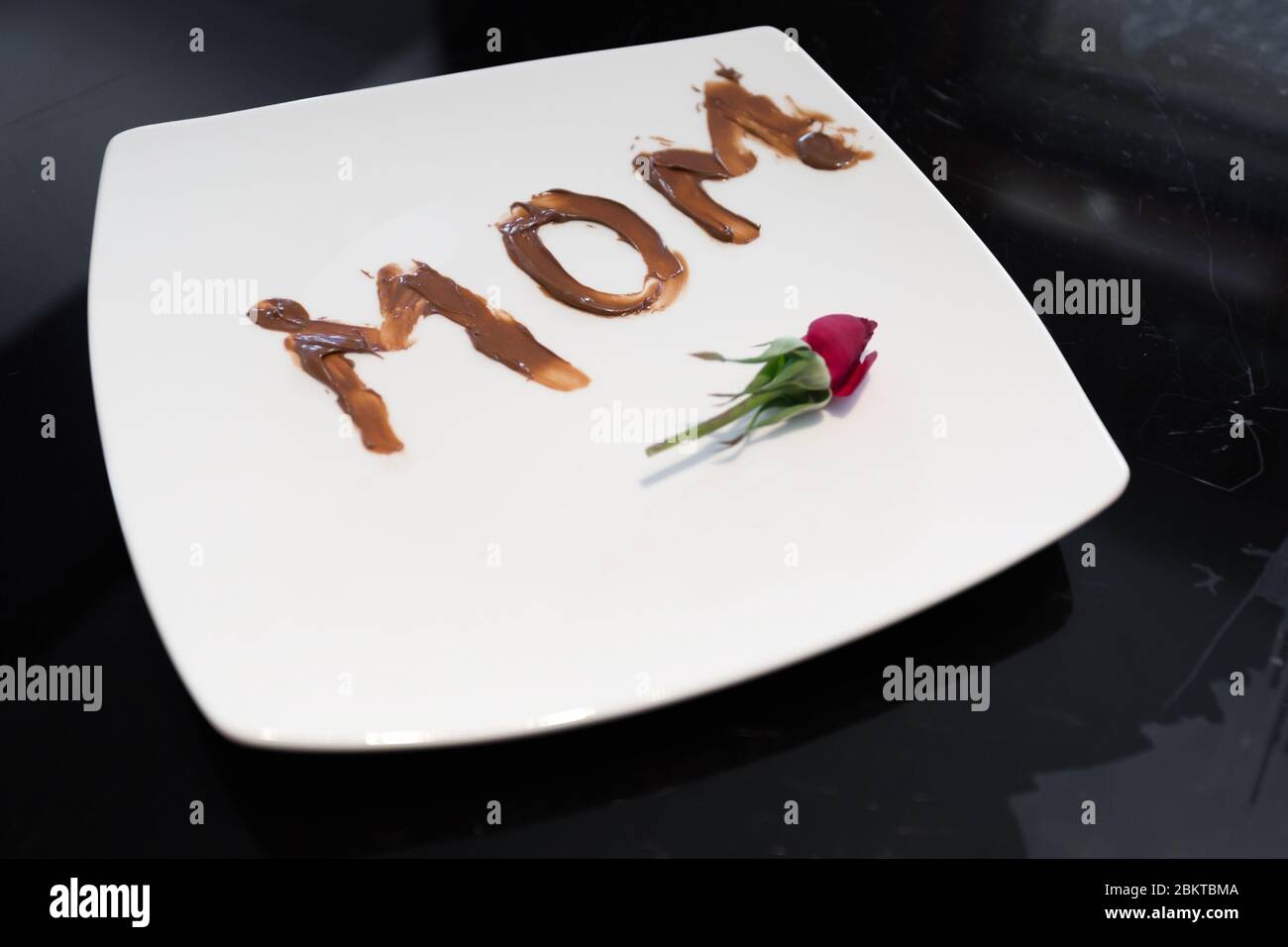 Le mot maman écrit sur une assiette avec du chocolat par sa jeune fille Banque D'Images