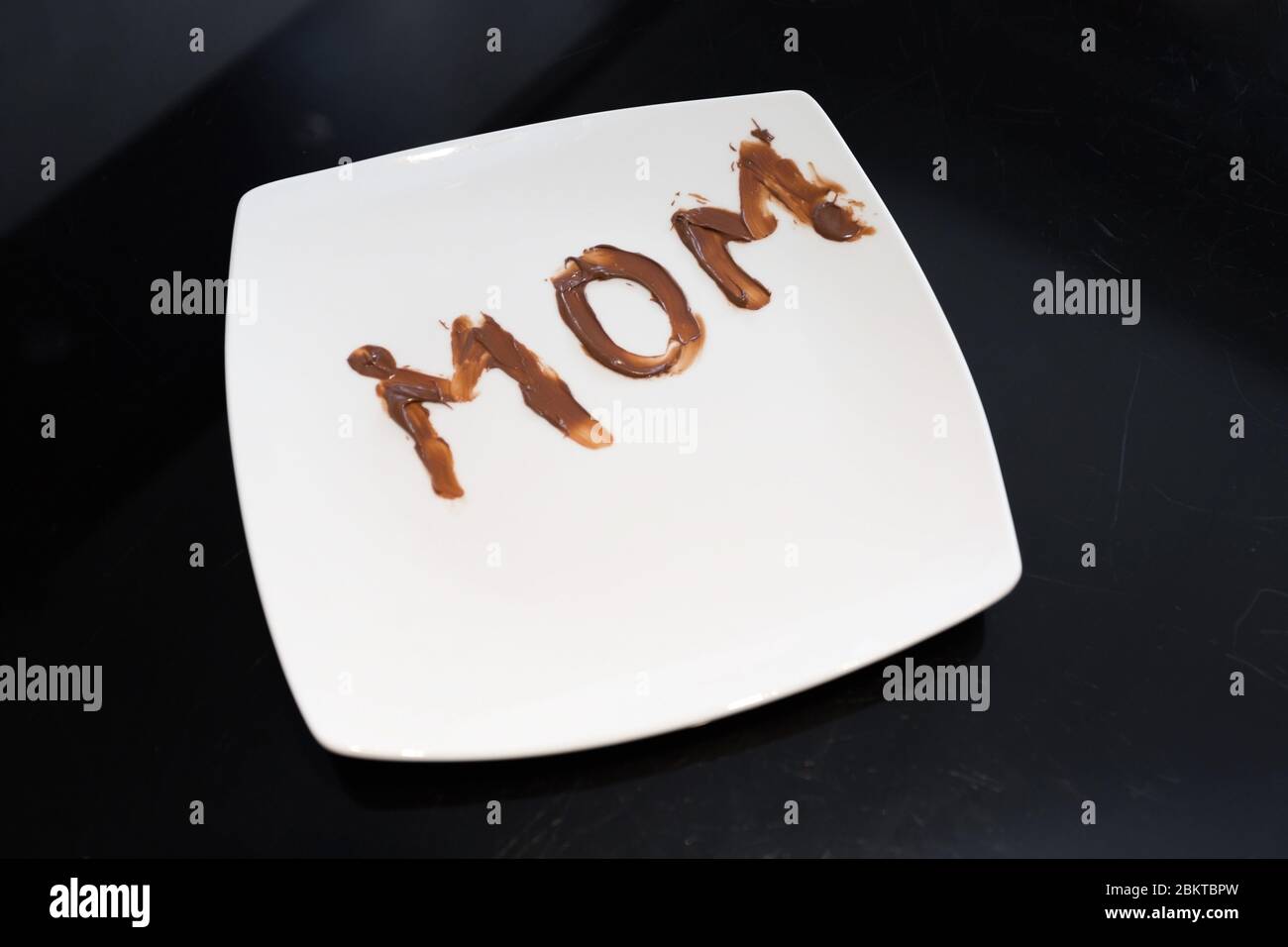 Le mot maman écrit sur une assiette avec du chocolat par sa jeune fille Banque D'Images