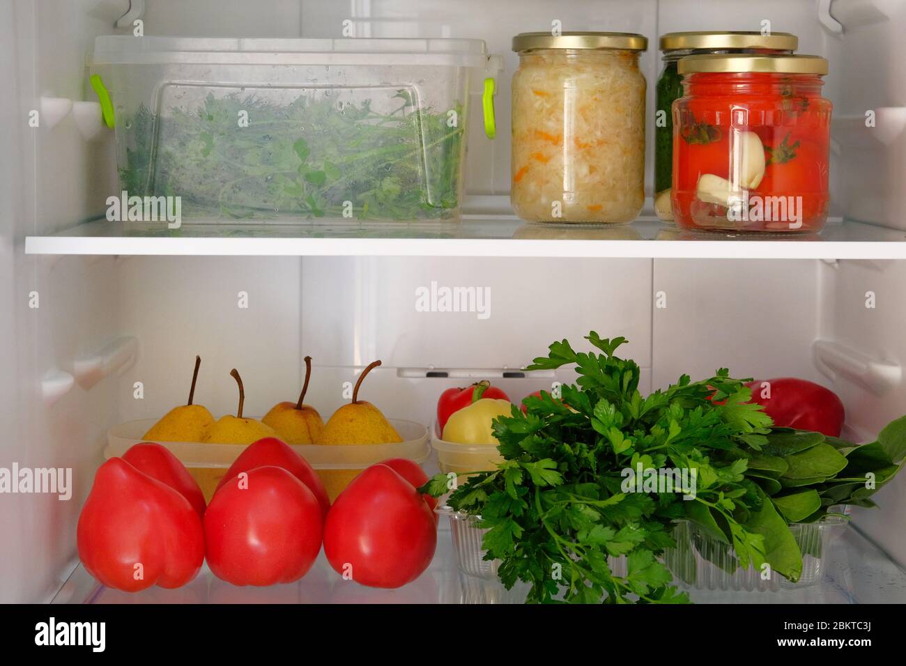 Ouvrez le réfrigérateur. Nourriture saine et fraîche poires, persil, concombres, tomates, poivre. Conserve dans le bol et les légumes sur la grille du réfrigérateur. Banque D'Images