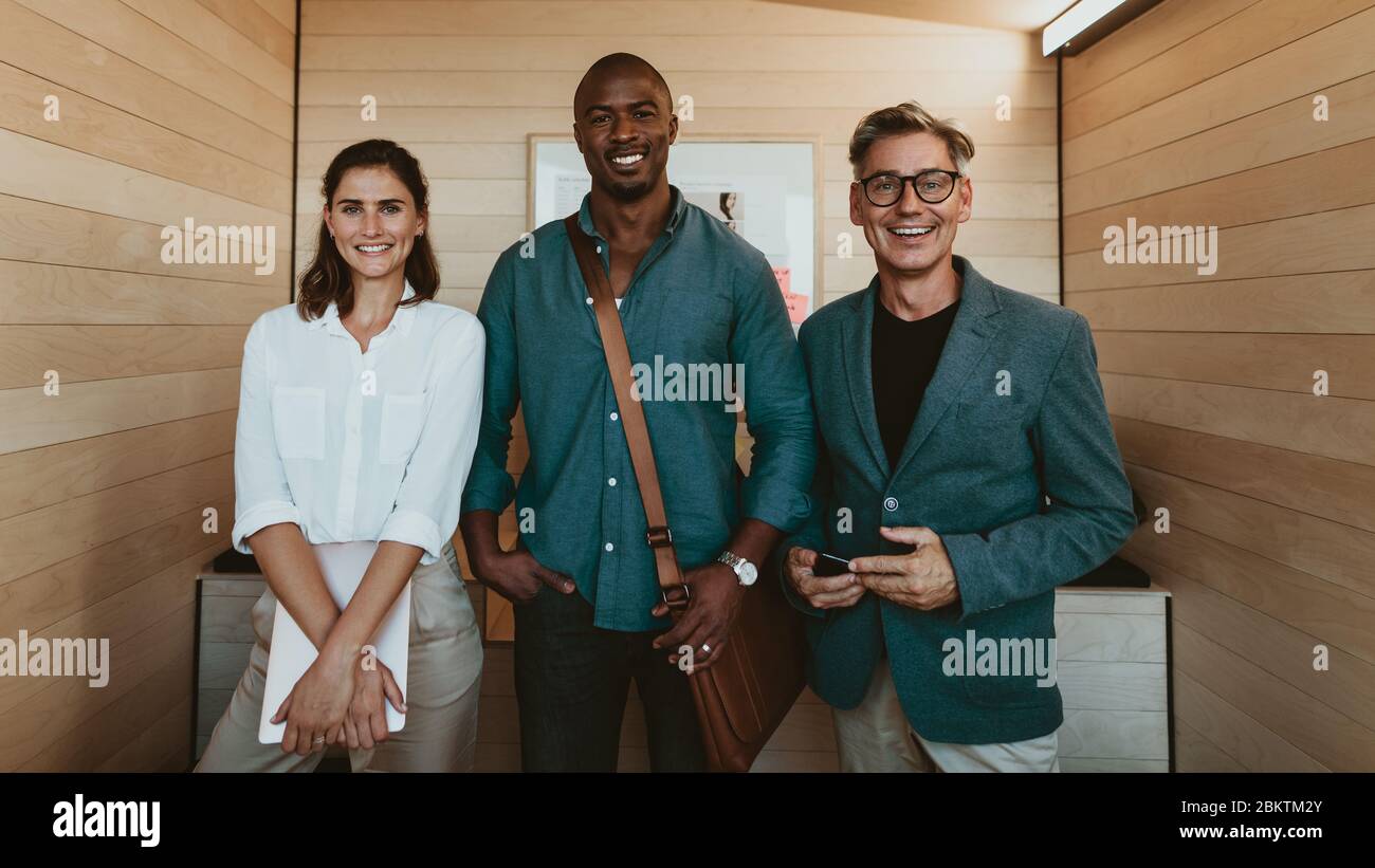 Groupe de professionnels d'affaires divers. Trois hommes d'affaires multiethniques se tenant ensemble au bureau, regardant la caméra et souriant. Banque D'Images