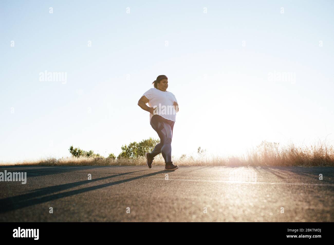 Femme de taille plus courant le matin. Femme en surpoids faisant de l'exercice matinal sur la route. Banque D'Images