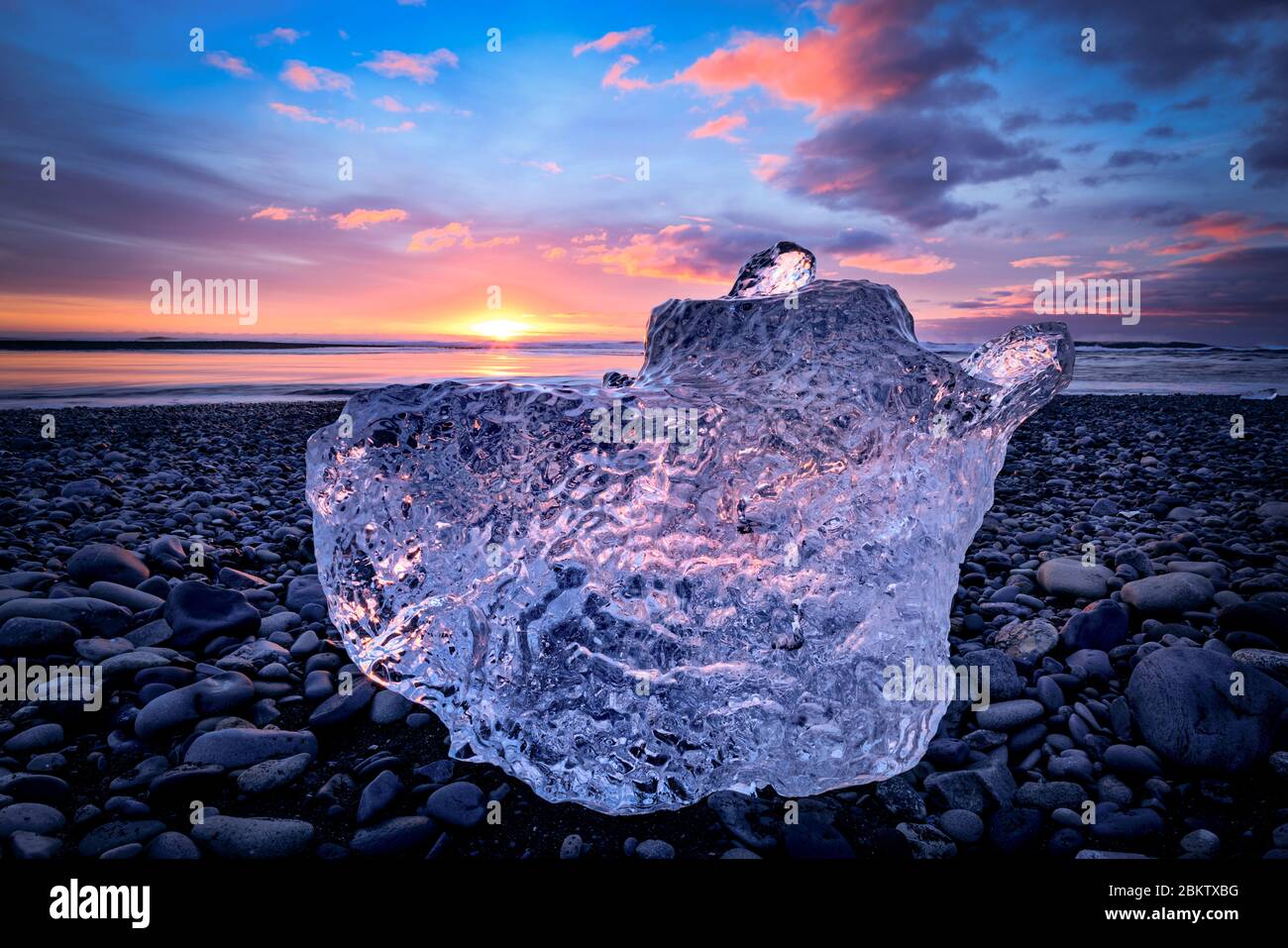 Une grande partie de glace assis sur la plage de sable noir avec le lever du soleil en arrière-plan. Banque D'Images