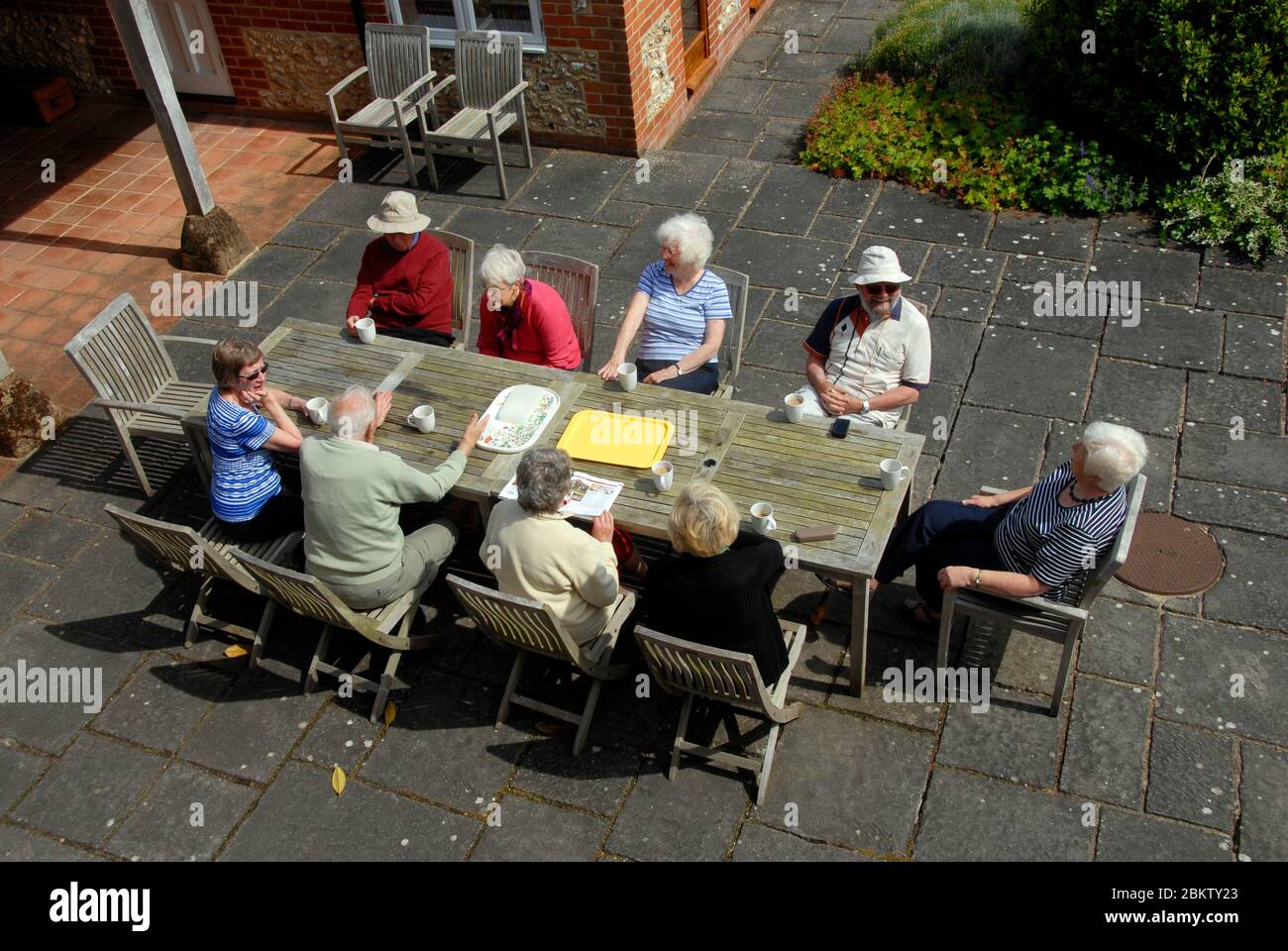 Groupe de neuf retraités assis autour d'une table ayant une discussion au soleil. Banque D'Images