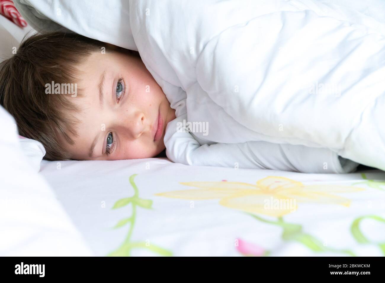 Garçon sous la couverture. Un enfant triste regarde par dessous les couvertures. Banque D'Images