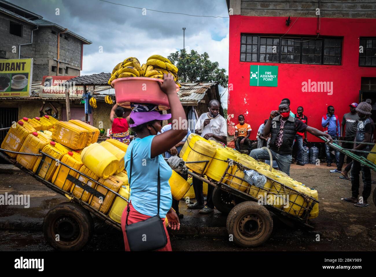 Nairobi, Kenya. 05e mai 2020. Un fournisseur de bananes passe devant un groupe de vendeurs d'eau locaux qui attendent en file pour remplir leurs canettes pendant la pénurie d'eau au milieu du couvre-feu en cours en raison de la pandémie du virus corona. Dans la plupart des quartiers et des rues de Kibera, les habitants de la région se promèneront à transporter leurs bidons d'eau vides à la recherche d'eau, tandis que certains doivent faire la queue pendant une longue période dans les parties où il y a accès à l'eau. Crédit : SOPA Images Limited/Alamy Live News Banque D'Images