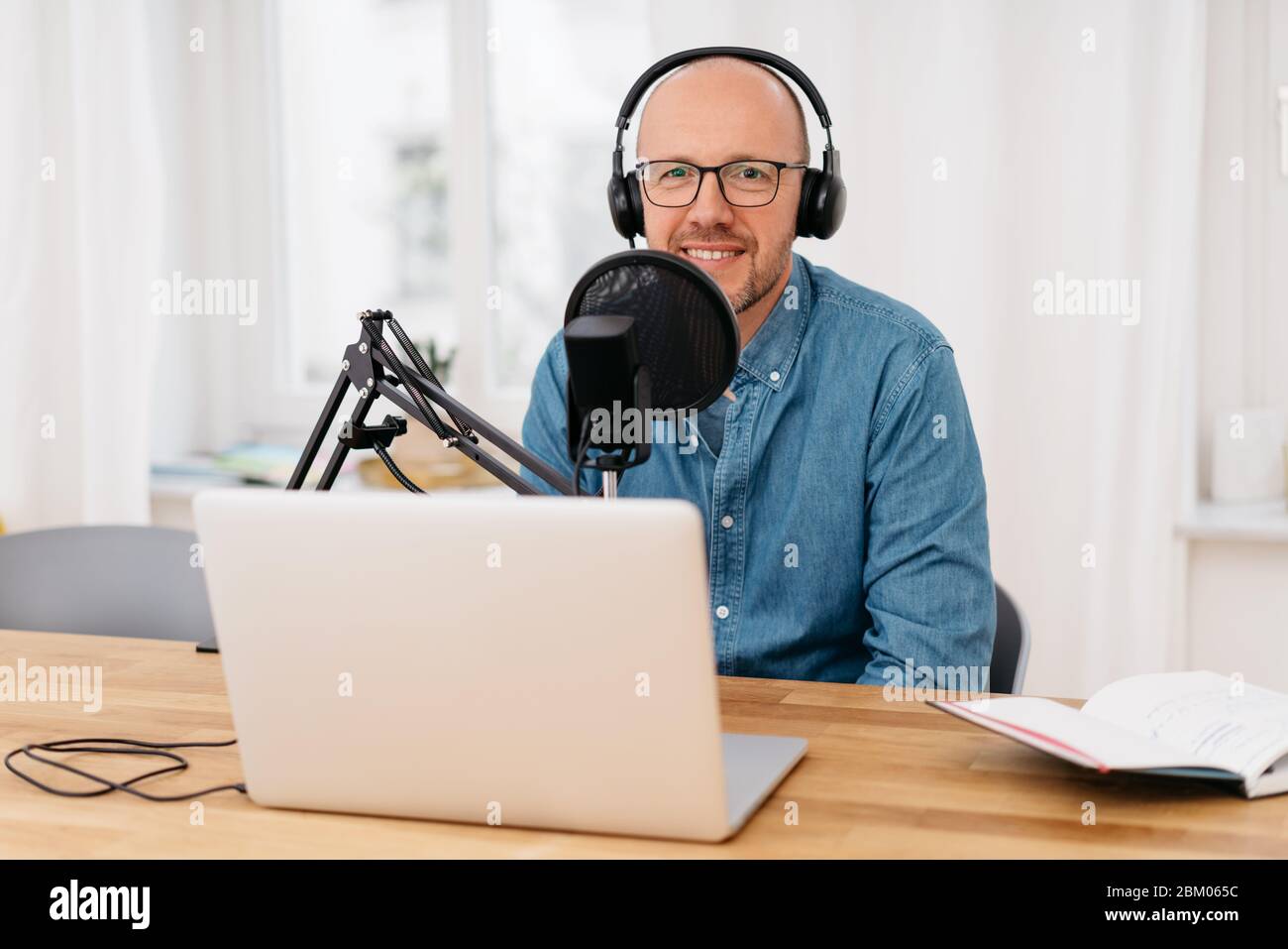 Homme souriant à la caméra pendant qu'il s'assoit à enregistrer un podcast  sur son ordinateur portable avec un casque et un microscope professionnel  Photo Stock - Alamy