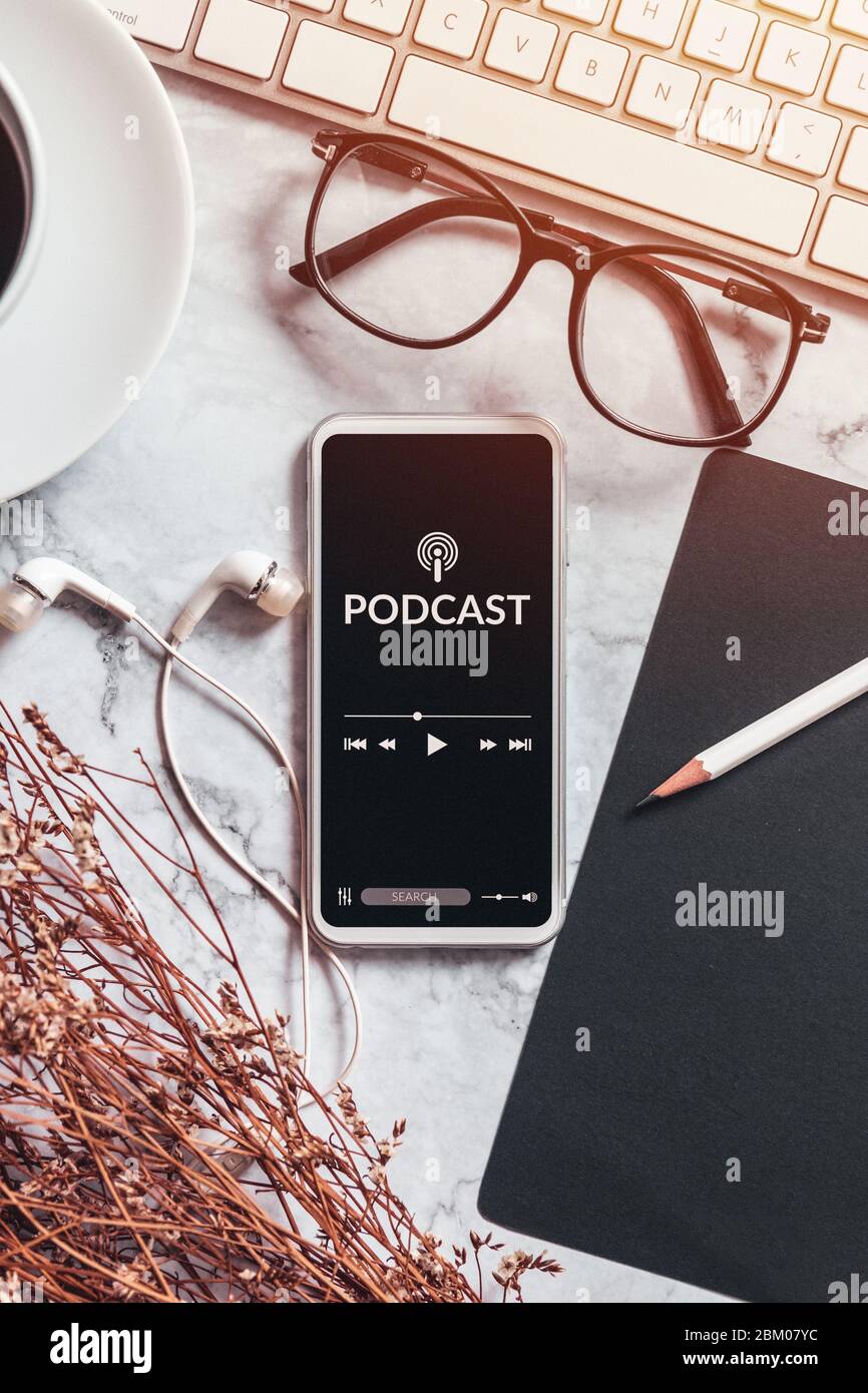 concept de contenu audio podcast. application podcast sur écran de smartphone mobile sur bureau avec tasse à café, écouteurs, lunettes, clavier d'ordinateur Banque D'Images