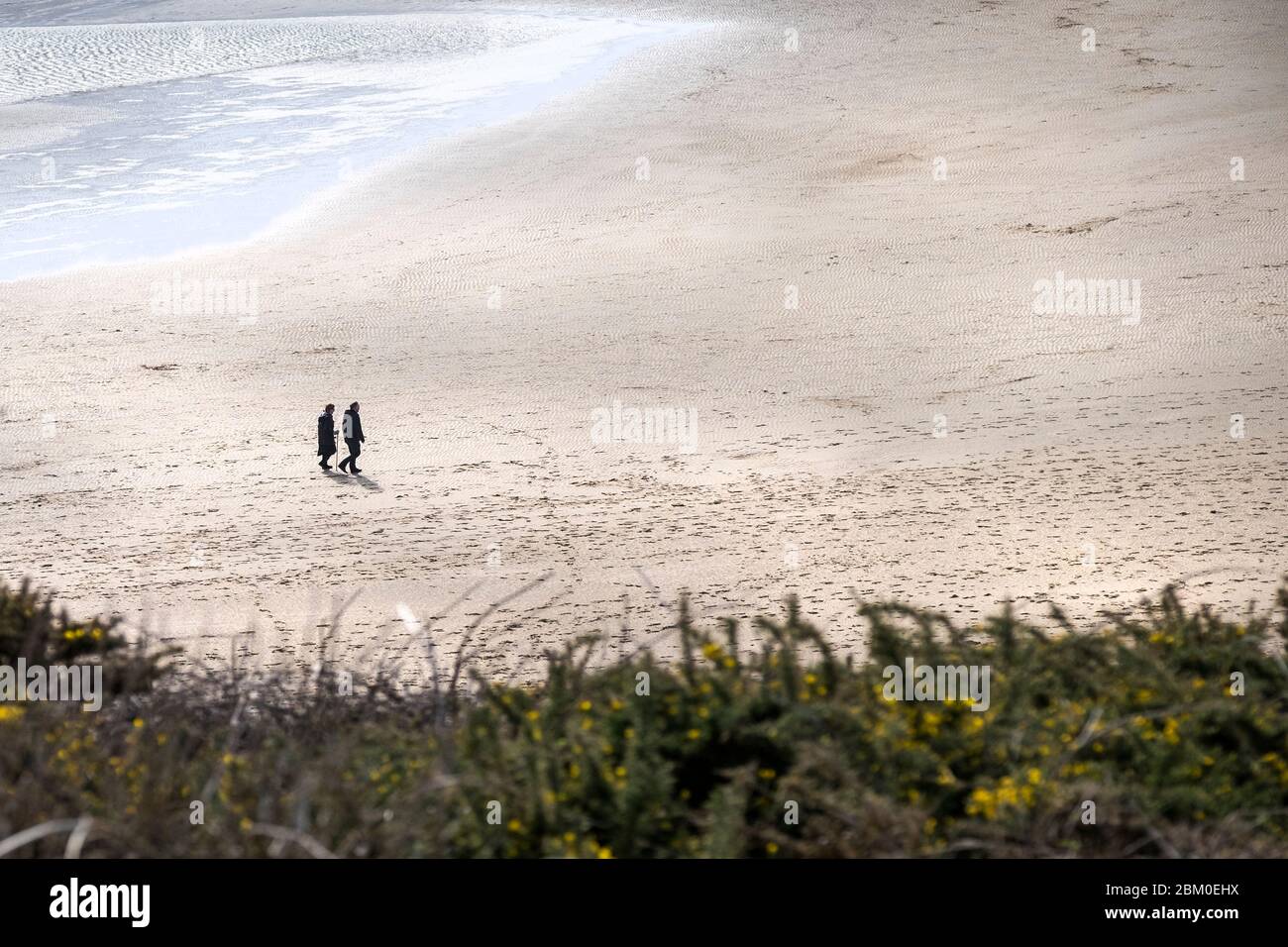 Vue lointaine de deux personnes traversant la plage primée Crantock Beach à marée basse à Newquay, en Cornouailles. Banque D'Images