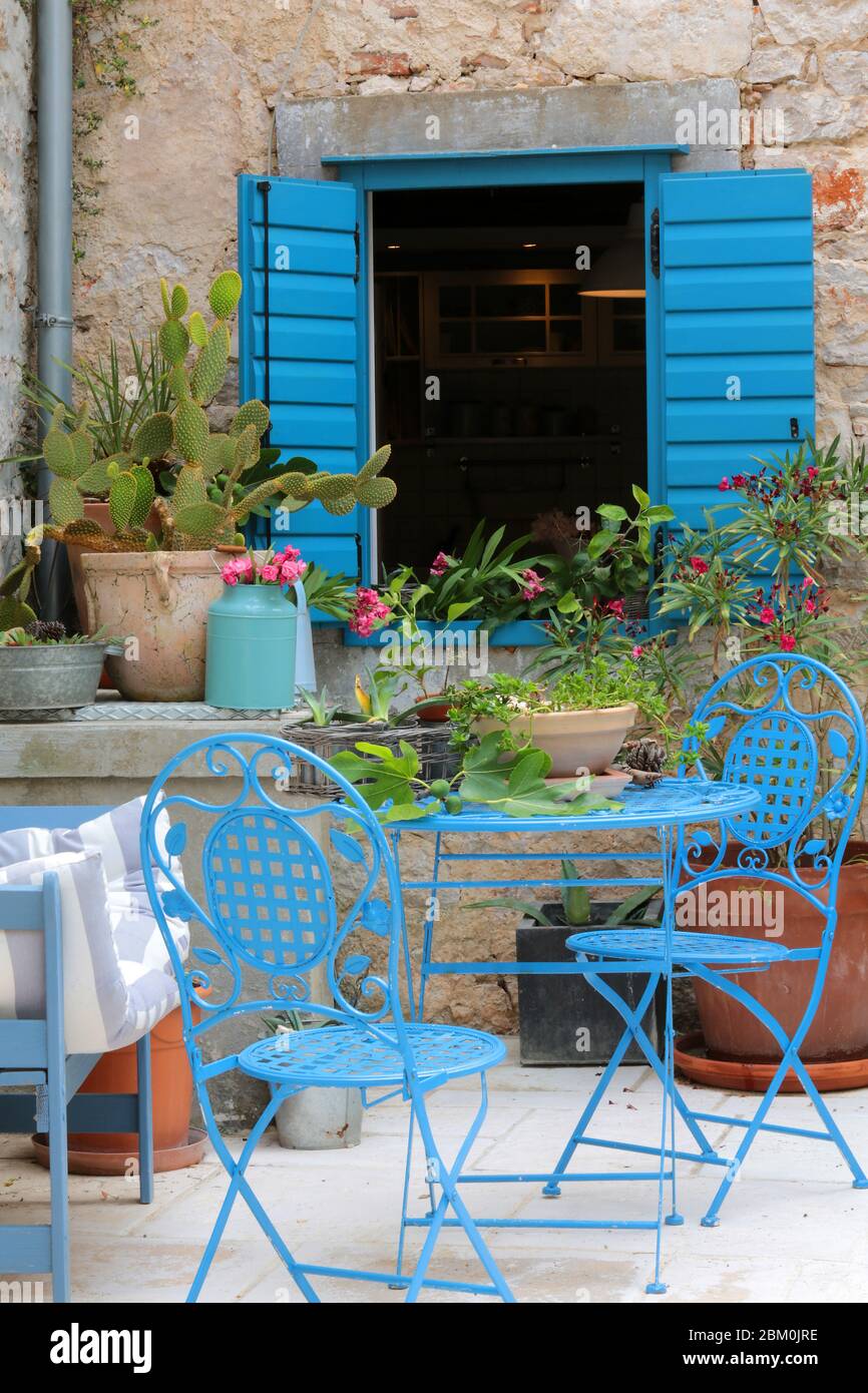 Une maison en pierre avec une fenêtre ouverte bleue et des chaises en face Banque D'Images