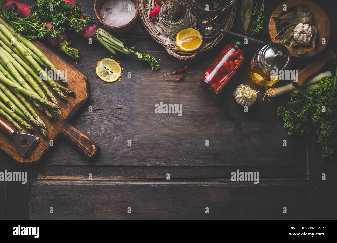 Fond de nourriture sombre avec asperges vertes et divers ingrédients et des pots avec légumes conservés, assaisonnement et outils de cuisine pour de savoureux recettes maison Banque D'Images