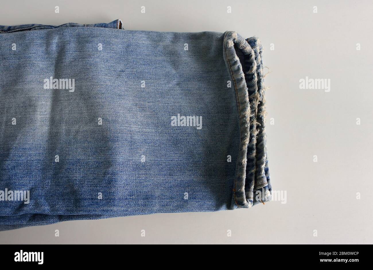 Gros plan et attention sélective sur les jambes effilochées d'une paire de jeans placée sur une table blanche rugueuse Banque D'Images