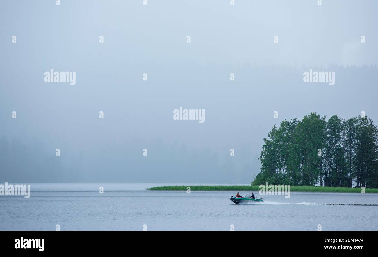 Petit hors-bord bateau à moteur / skiff conduisant au lac Kallavesi à une forte averse , Kuopio , Finlande Banque D'Images