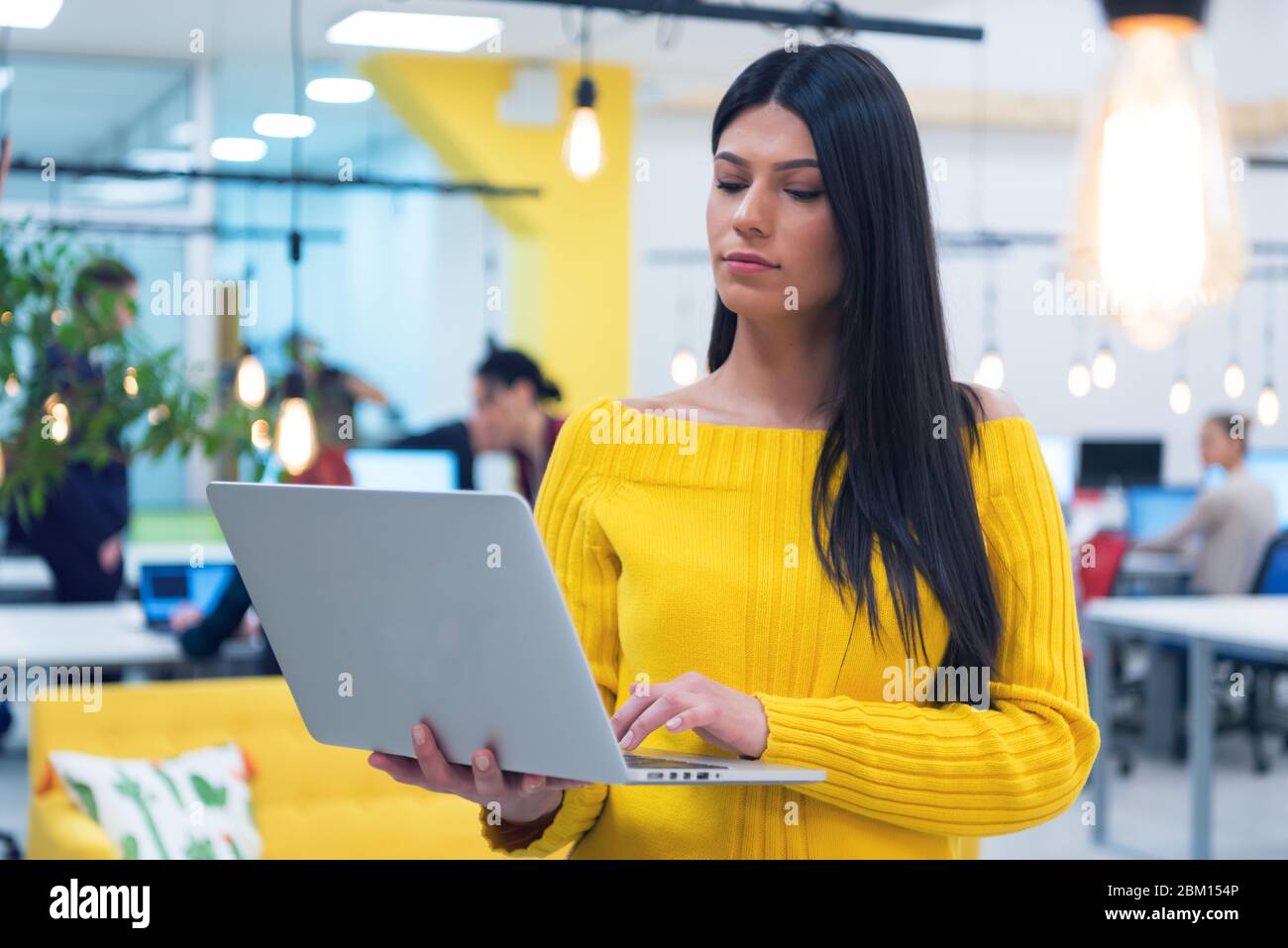 Portrait d'une jeune femme d'affaires décontractée et heureuse debout avec un ordinateur portable sur son lieu de travail dans un espace de travail moderne. Banque D'Images