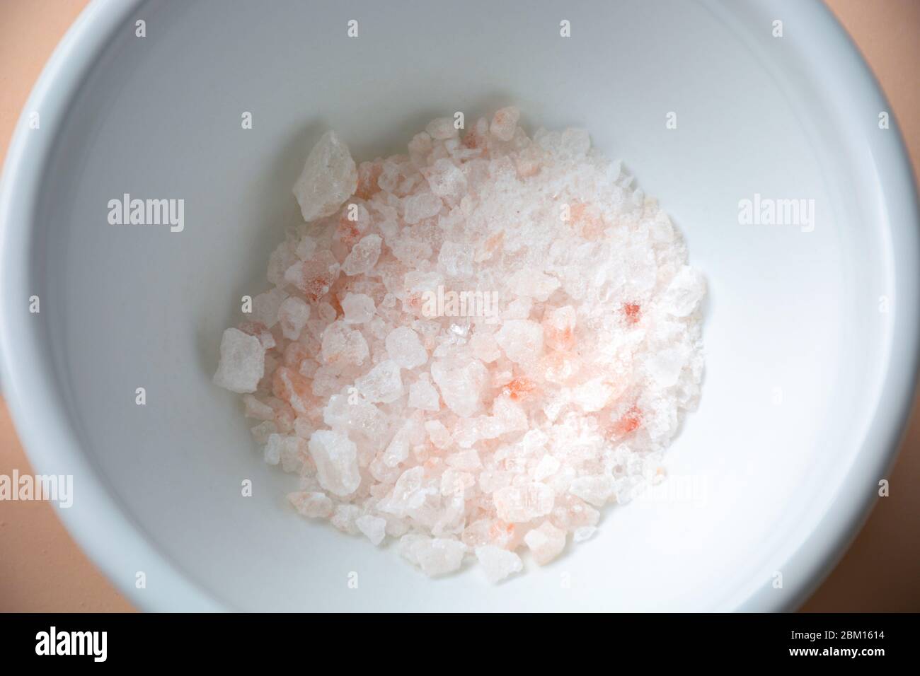 Cristaux de sel de roche rose himalayen écrasés dans un mortier de bol blanc en céramique Banque D'Images