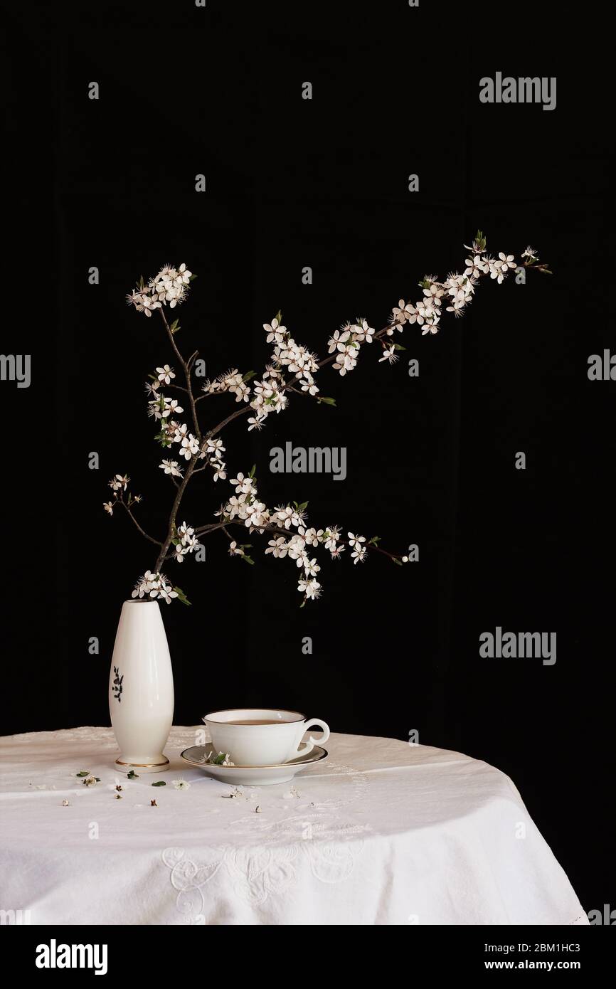 Table noire et blanche en ambiance printanière. Branche d'arbre en fleur dans un vase et une tasse de thé sur une table blanche Banque D'Images