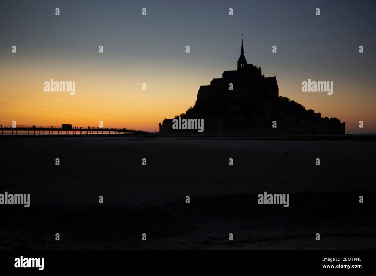 Silhouette du Mont Saint Michel au coucher du soleil, France. Les gens marchent sur le pont pour visiter le monastère. Banque D'Images