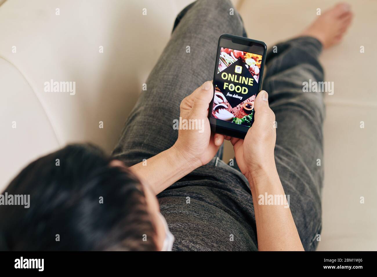 Gros plan d'un jeune homme qui se repose sur un canapé, vérifie l'application du café et choisit ce qu'il faut commander en ligne pour le dîner Banque D'Images
