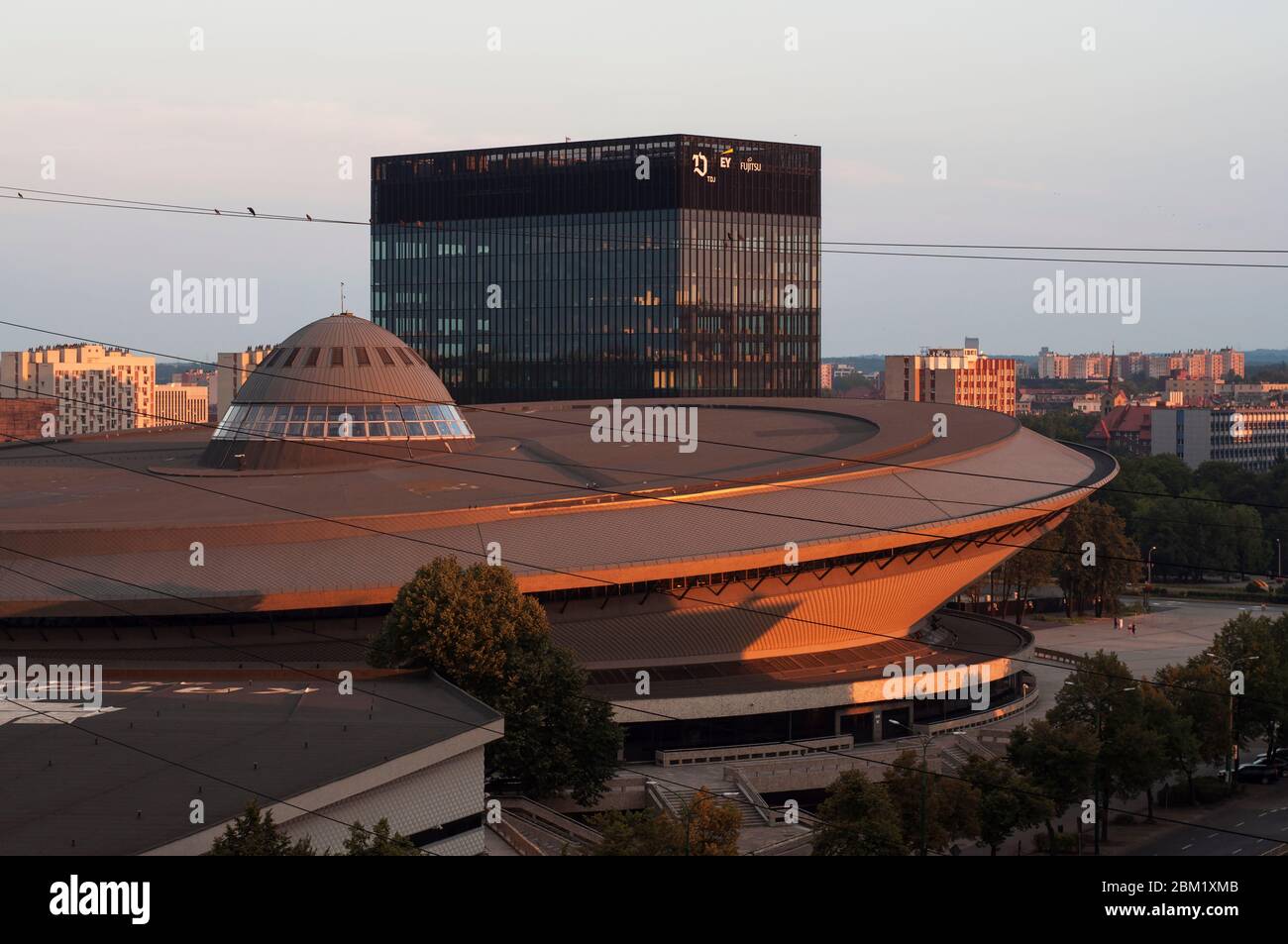 Salle de sport et de divertissement Spodek à Katowice derrière laquelle se dresse un immeuble de bureaux moderne au lever du soleil Banque D'Images