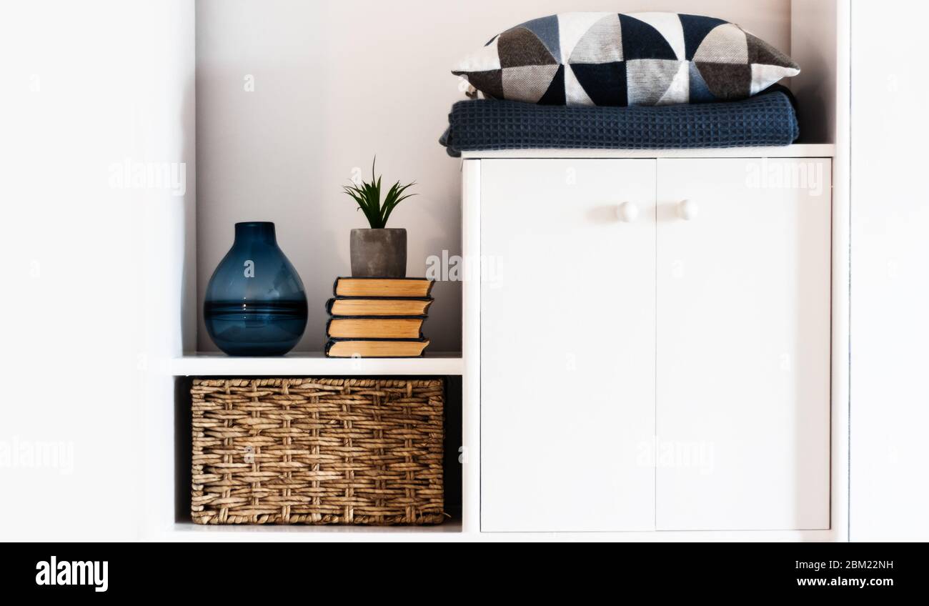 Décoration intérieure chaleureuse : oreiller, écossais, vase bleu, pile de livres, plante en pot, boîte en osier sur une étagère blanche dans la chambre. Le concept de quarantaine de s. Banque D'Images