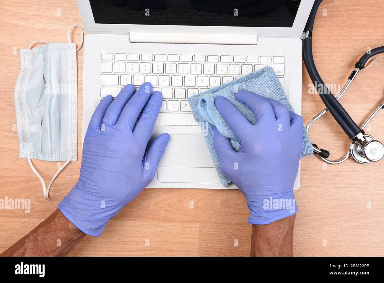 Professionnel de la santé avec des mains gantées désinfectant un clavier d'ordinateur portable contre les virus, microbes et la saleté. CovID-19 prévention. Banque D'Images