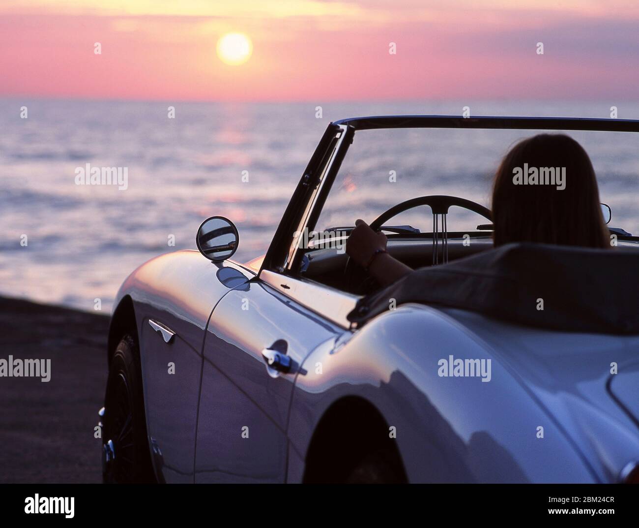 Jeune femme conduisant à gauche 1965 Austin Healey 3000 au coucher du soleil sur la route côtière dans le Kent Banque D'Images