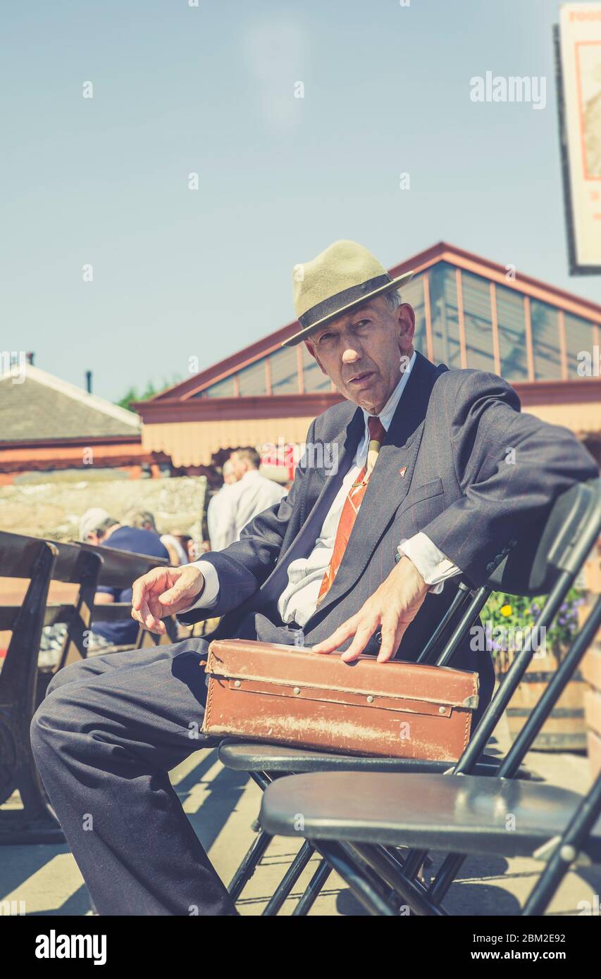 Homme des années 1940 en chapeau assis sous le soleil d'été, Kidderminster gare d'époque, Severn Valley Railway, Royaume-Uni. Banque D'Images