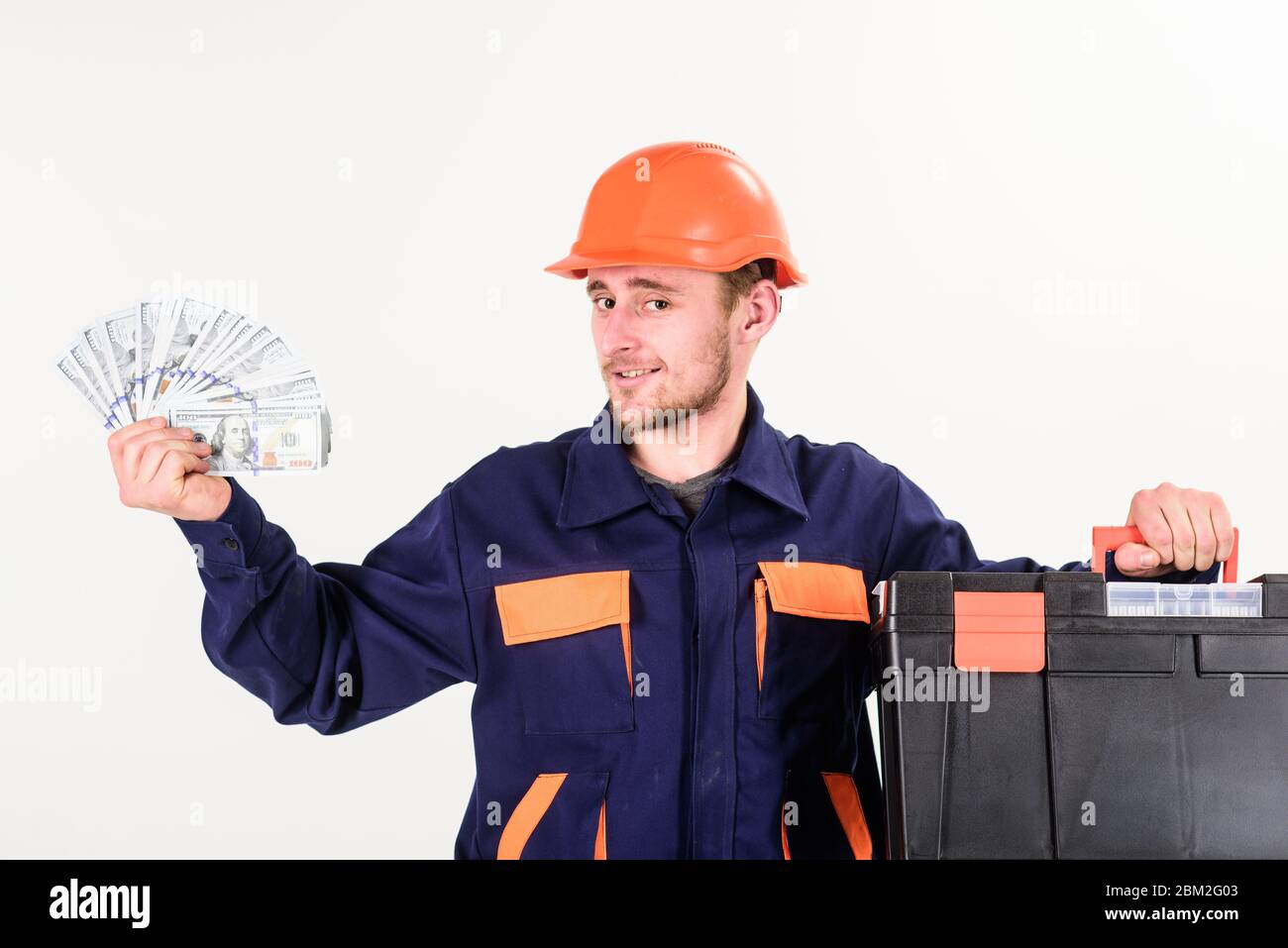 L'homme avec la boîte à outils a obtenu le salaire, l'argent pour le travail. Le constructeur gagne de l'argent, le réparateur garde de l'argent, des billets en main. Homme de main avec visage souriant dans un casque sur fond blanc. Concept de service et de paiement. Banque D'Images