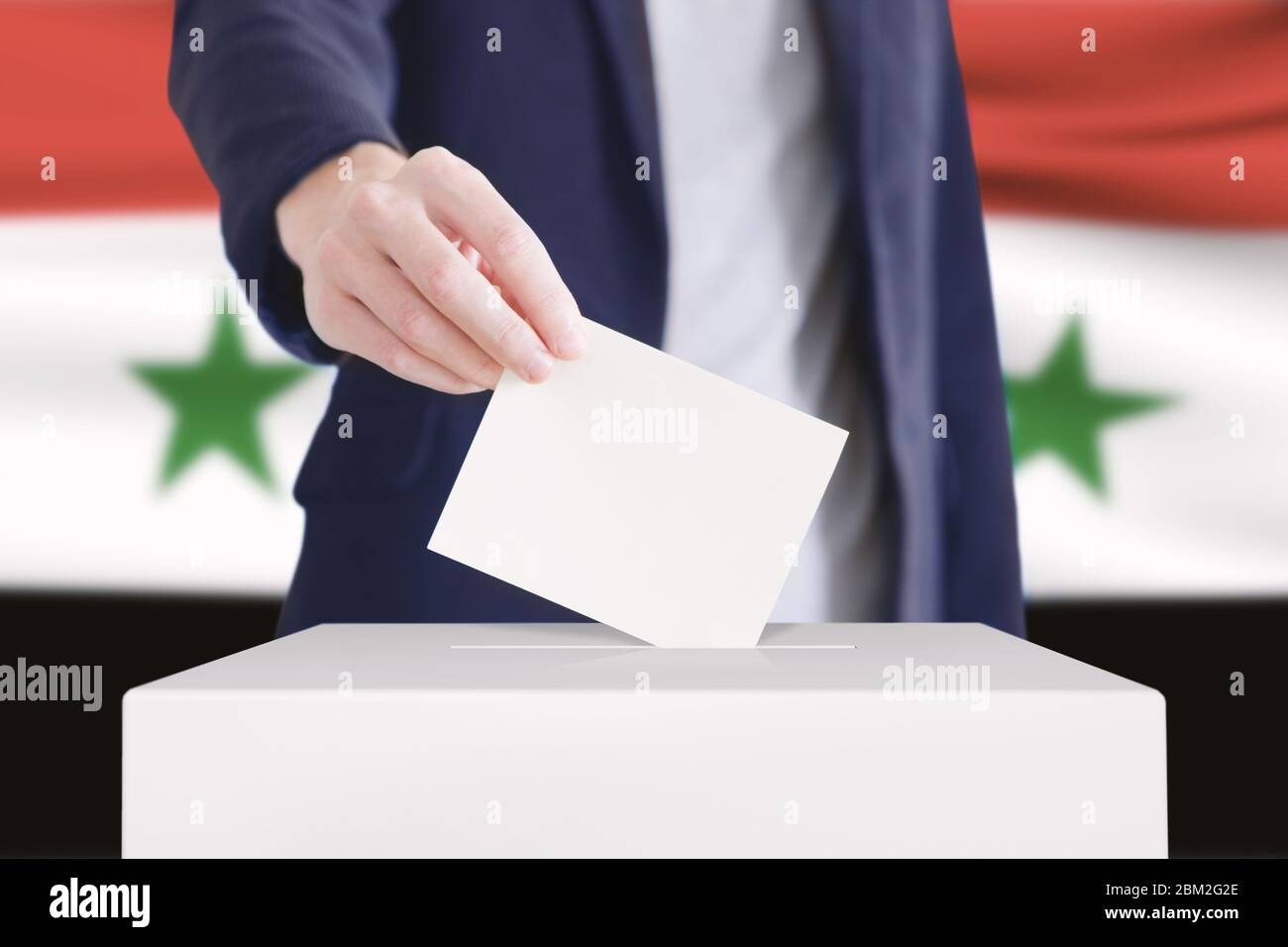 Homme mettant un bulletin de vote dans une boîte de vote avec le drapeau syrien sur fond. Banque D'Images