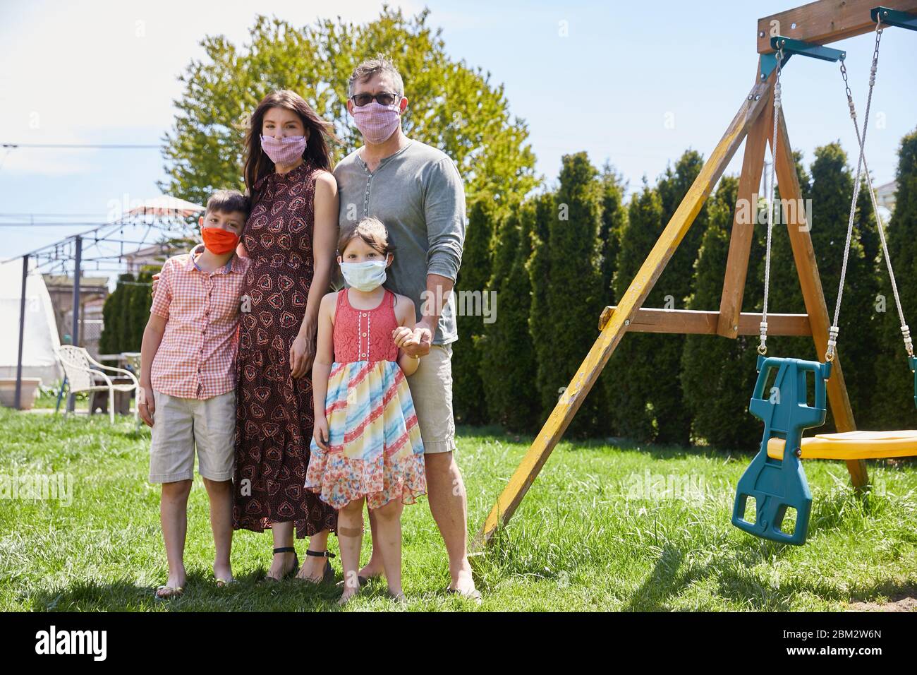 Une famille se tient en solidarité à l'extérieur d'un parc portant des masques faciaux pour prévenir l'infection par le coronavirus Banque D'Images