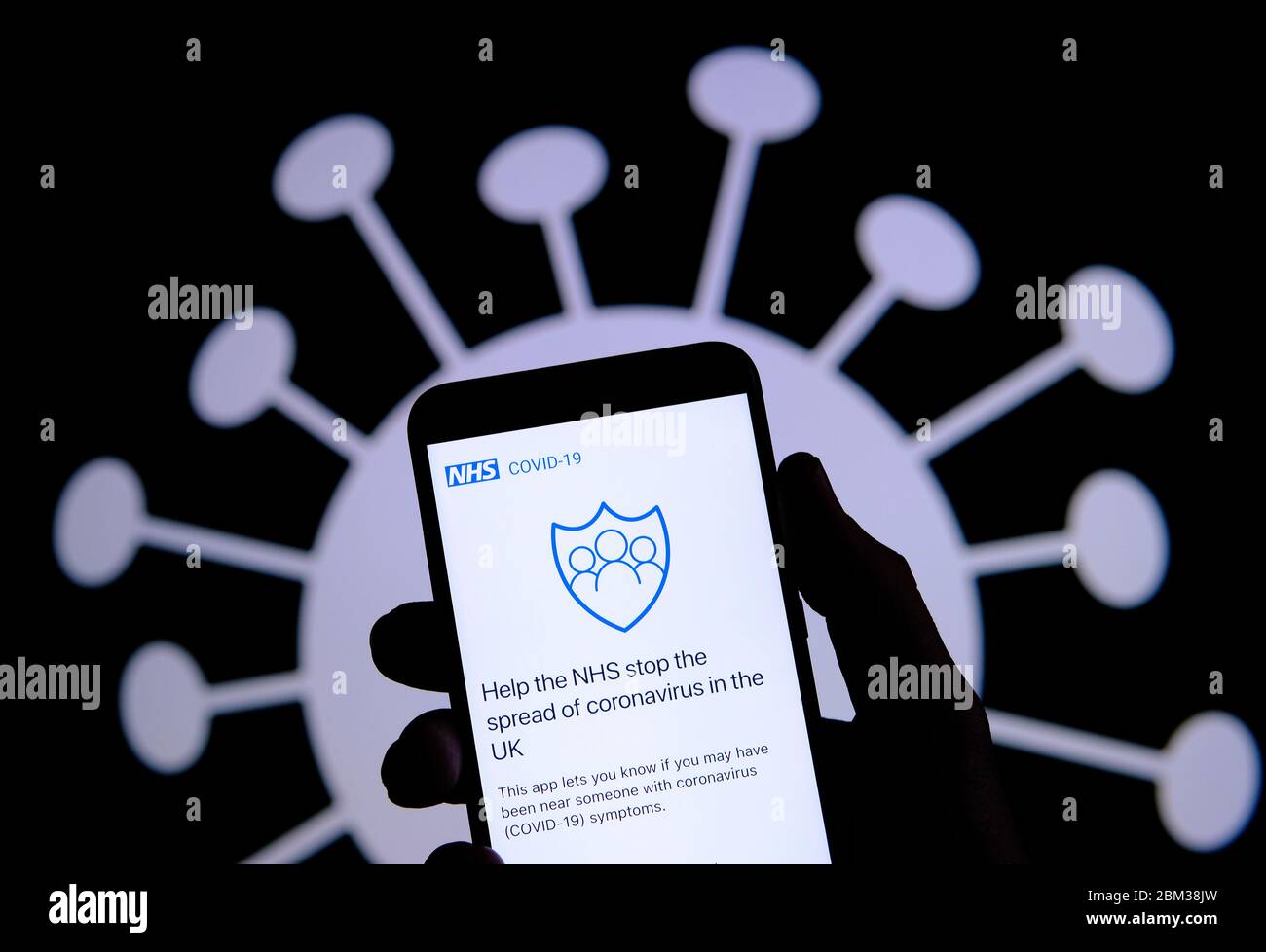 Stone / Royaume-Uni - Mai 6 2020: NHS COVID-19 contact-tracing app sur la silhouette de smartphone tenir dans une main. Image du coronavirus sur l'ba floue Banque D'Images