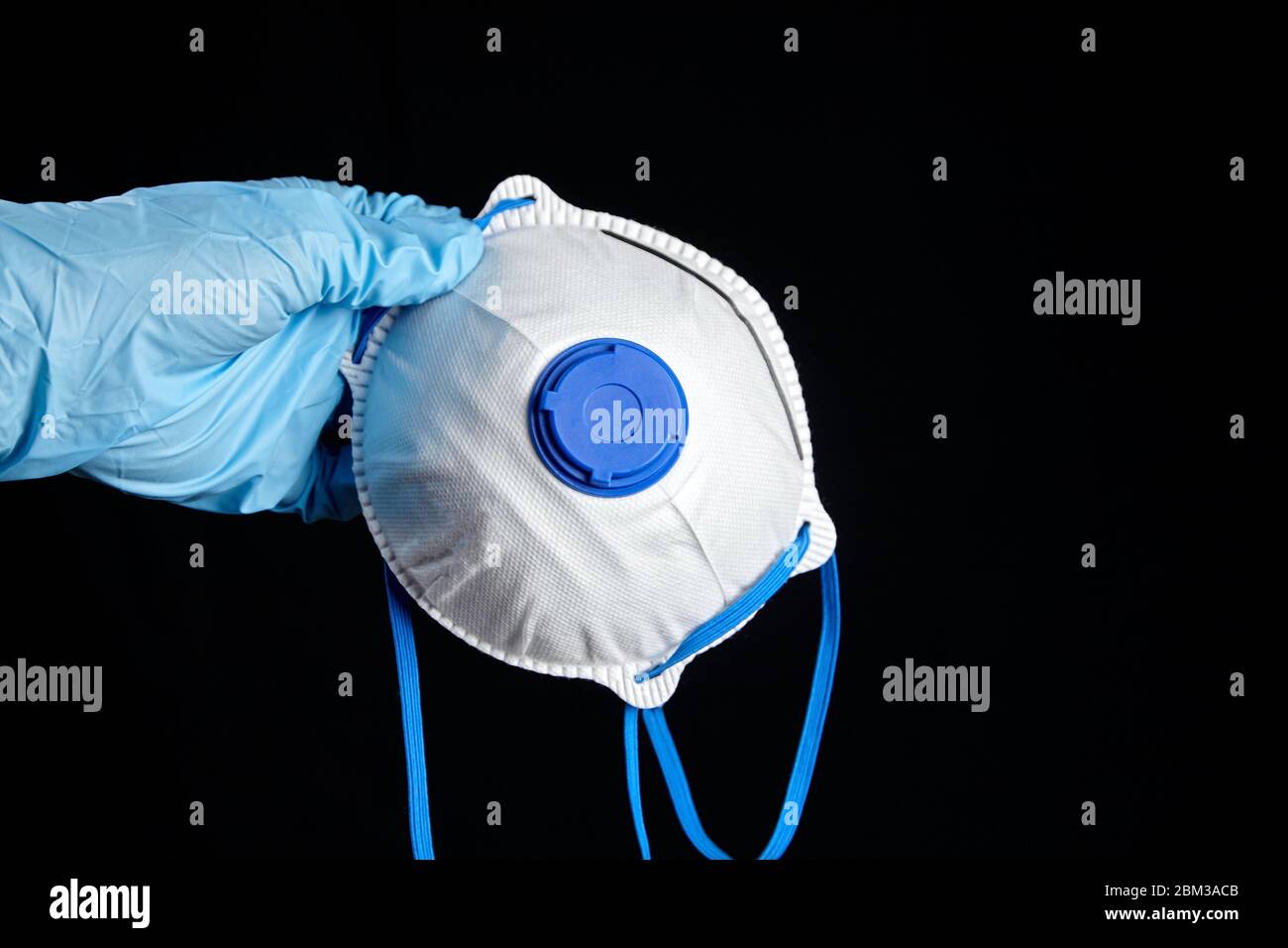Masque filtrant à la main, gants bleus, isolé sur fond noir. Masque N95. Masque FFP2 blanc, protection contre le coronovi Banque D'Images