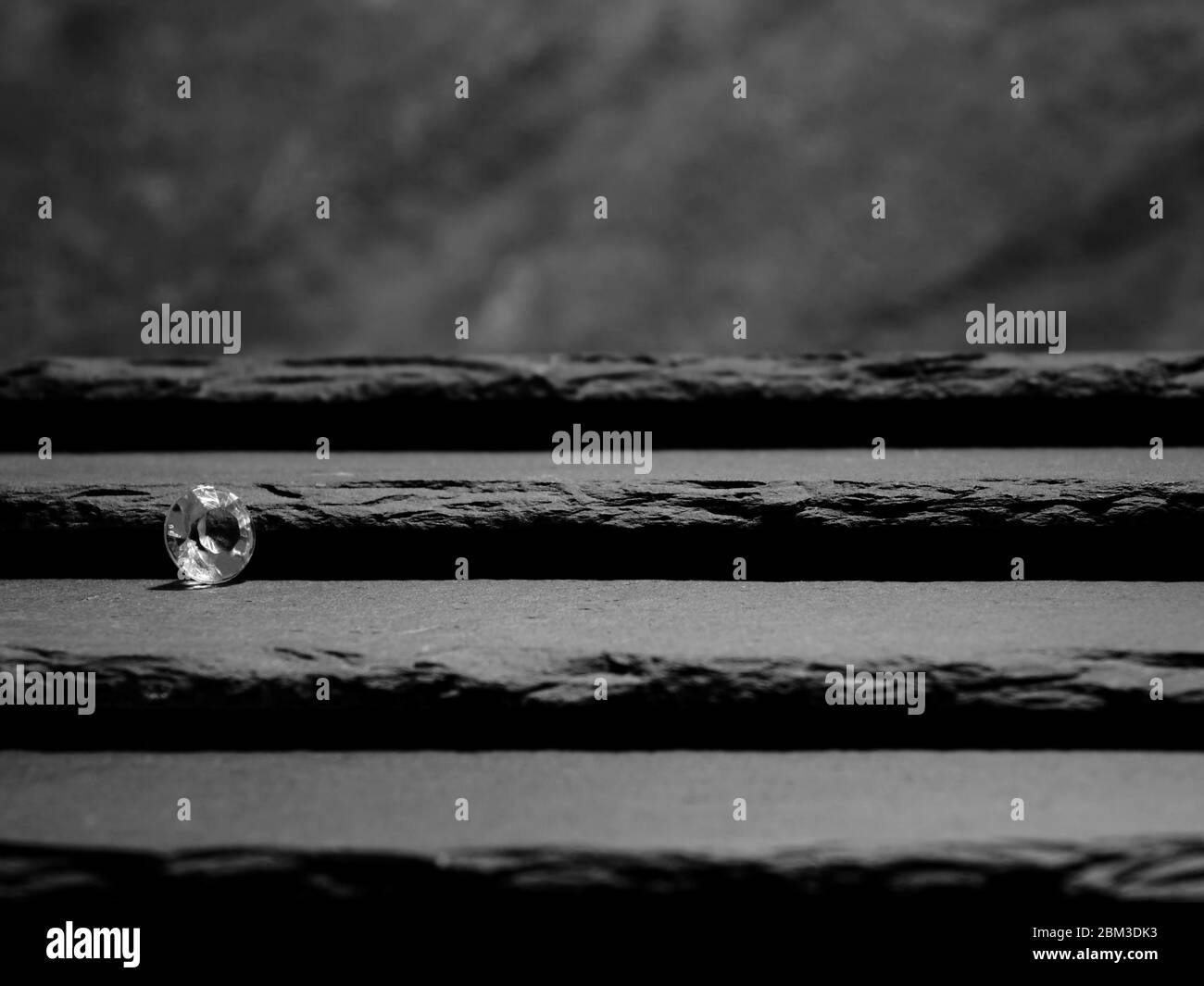 Un diamant unique affichant la coupe de la pierre à facettes, posée sur des marches en ardoise menant à un fond flou de roche Banque D'Images