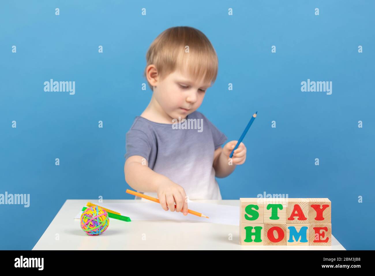 Beau garçon blond flou dessine avec des crayons de couleur sur des feuilles de papier sur une table blanche. Concept rester à la maison à cause de la quarantin du coronavirus Banque D'Images