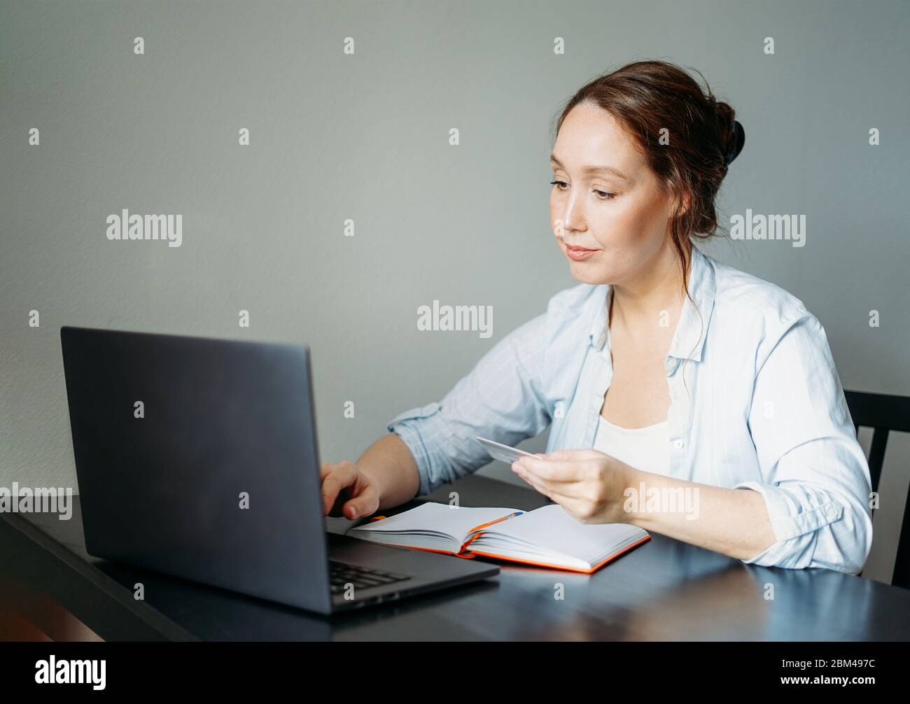 La femme brune souriante adulte effectue des paiements par carte de crédit par ordinateur portable ouvert à la maison Banque D'Images