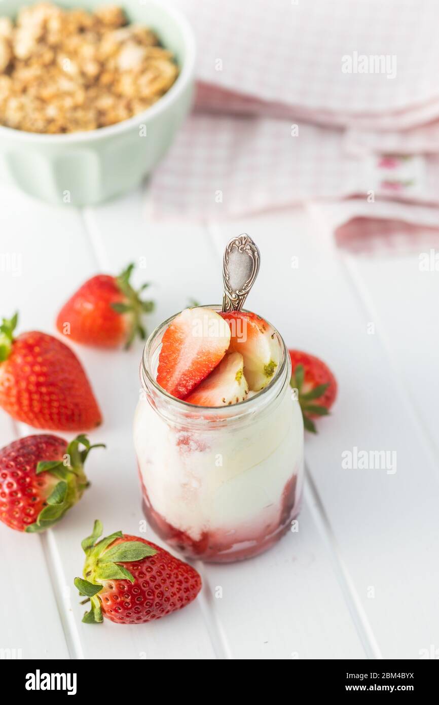 Yaourt blanc fruité dans un pot et fraises sur table blanche. Banque D'Images