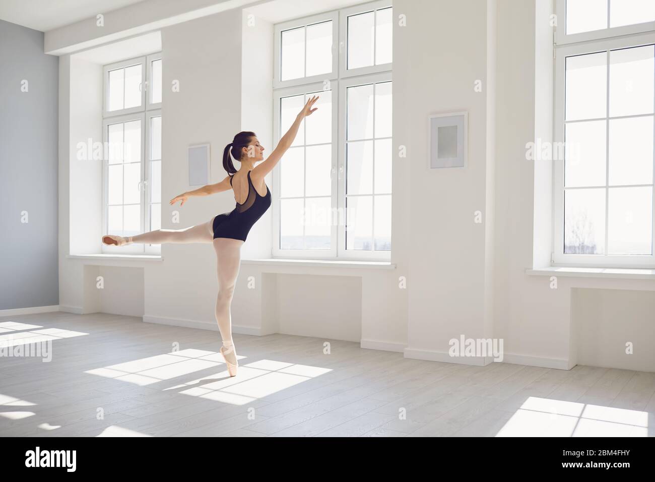 Ballerine. La jeune danseuse de ballet élégante répète une performance dans un studio blanc avec des fenêtres. Répétition de danse en classe studio. Banque D'Images