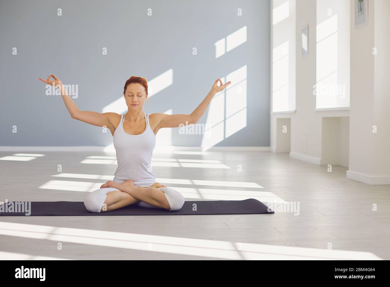 Yoga girl woman.Fitness girl pratique le yoga dans une position lotus assis sur un sol gris dans un studio lumineux blanc. Banque D'Images
