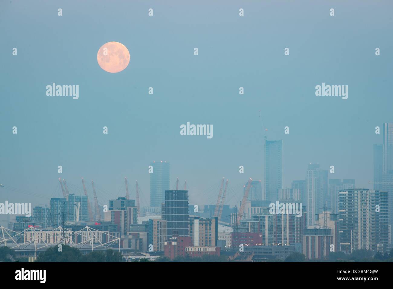 La lune se couche sur l'O2 Arena et de grands bâtiments dans l'est de Londres. La pleine lune de mai est également connue sous le nom de 'lune de fleur', signifiant les fleurs qui fleurissent pendant le mois. Banque D'Images