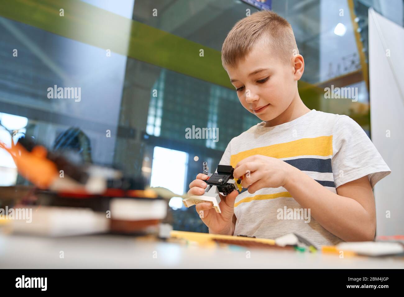 Vue de face du kit de construction pour le groupe d'enfants créant des jouets, ayant des émotions positives et de la joie. Attention sélective de charmant garçon caucasien travaillant sur le projet, prenant des parties colorées. Banque D'Images