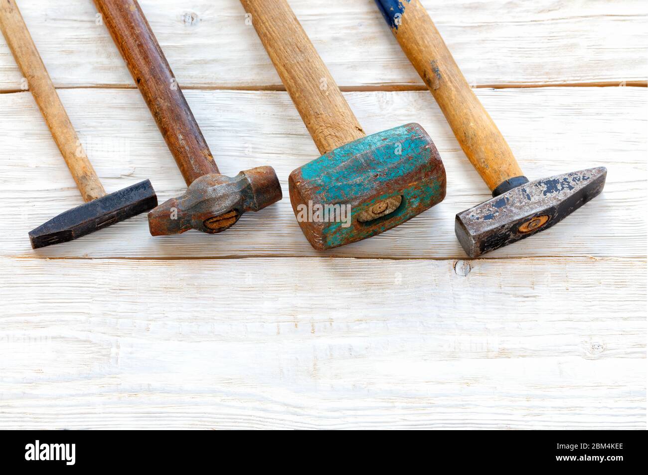 Les marteaux en fer usés avec poignées en bois sont posés en diagonale sur une table en bois blanc, vue du dessus, espace de copie. Banque D'Images