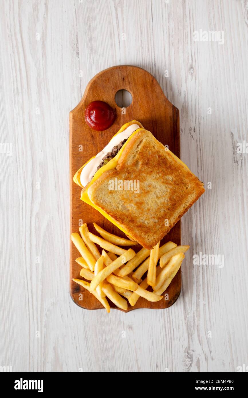 Hamburger au fromage frais grillé et frites sur un panneau de bois rustique sur une surface en bois blanc, vue du dessus. Pose à plat, en hauteur, par le dessus. Banque D'Images