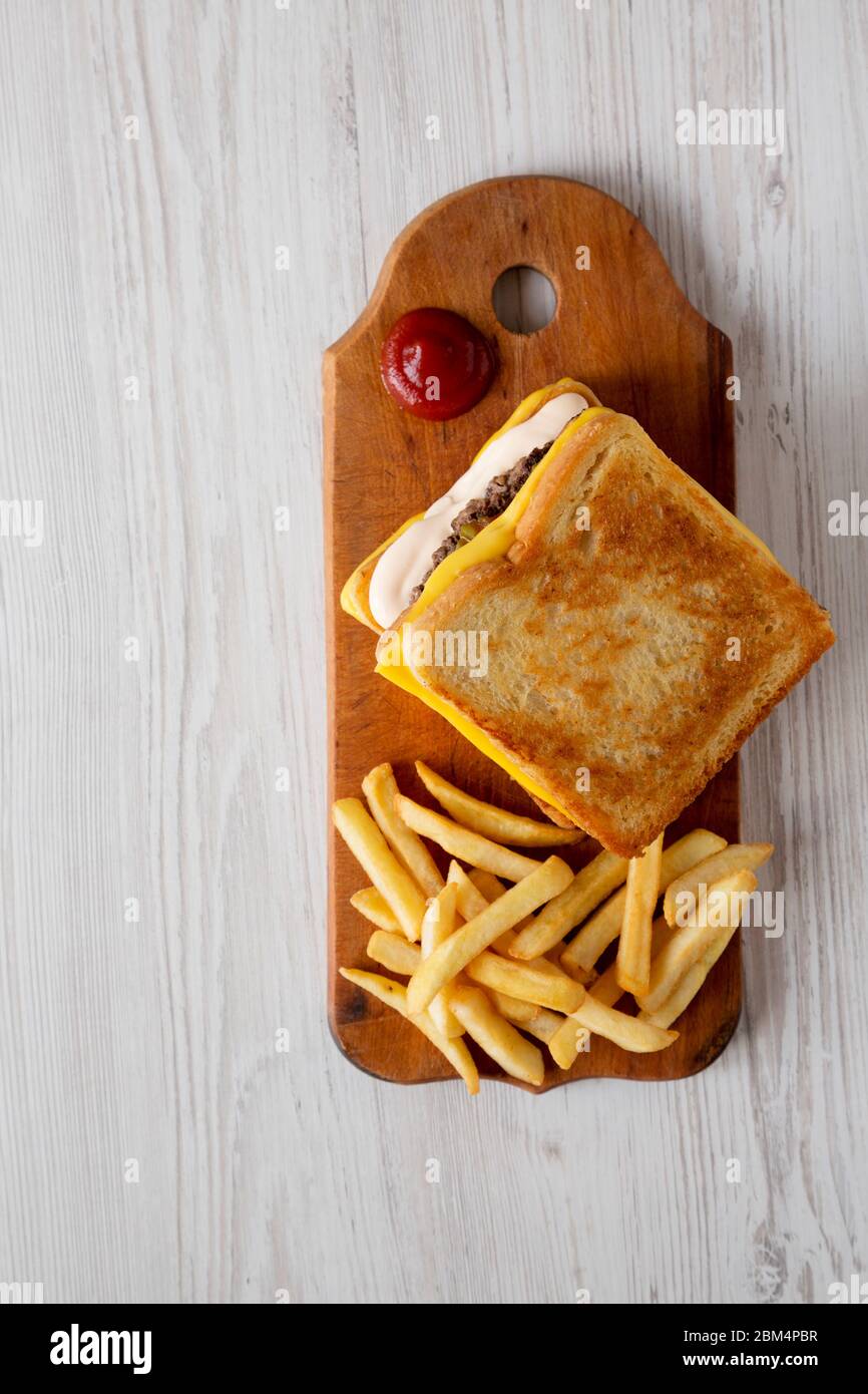 Hamburger au fromage frais grillé et frites sur un panneau de bois rustique sur fond de bois blanc, vue du dessus. Pose à plat, en hauteur, par le dessus. Copier sp Banque D'Images