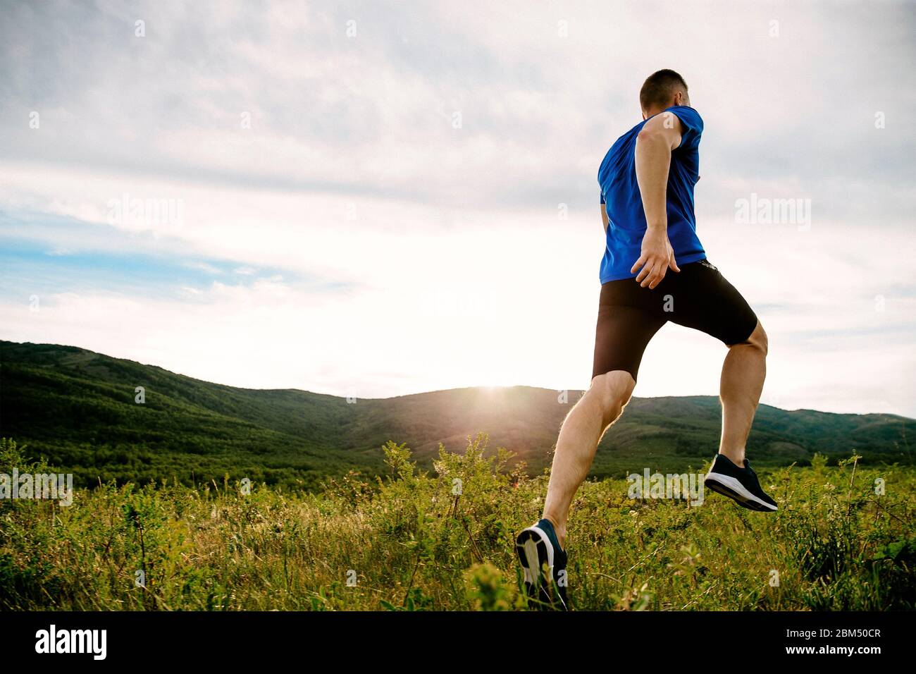 le coureur sportif s'exécute sur un sentier de montagne au coucher du soleil d'été Banque D'Images